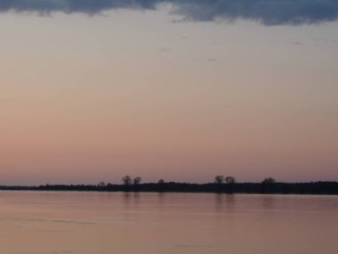 Pembe renklerle güzel, berrak gün batımı. Ayrıca üzerinde ağaçların yansıması olan bir nehir de var..
