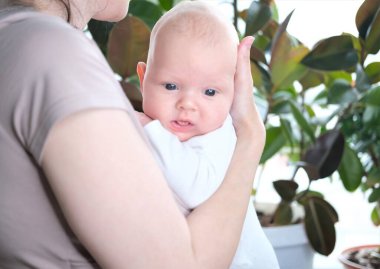 Güzel, genç bir anne yeni doğmuş oğlunu pencerenin kenarında kollarında tutuyor. Bir çocuğun yakın plan portresi