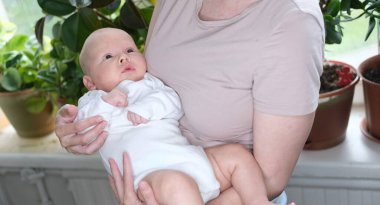 Güzel, genç bir anne yeni doğmuş oğlunu pencerenin kenarında kollarında tutuyor. Bir çocuğun yakın plan portresi