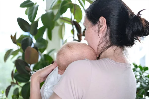 Güzel, genç bir anne yeni doğmuş oğlunu pencerenin kenarında kollarında tutuyor. Bir çocuğun yakın plan portresi