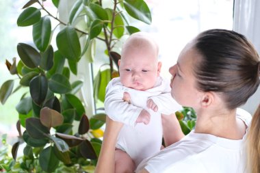Güzel, genç bir anne yeni doğmuş oğlunu pencerenin kenarında kollarında tutuyor. Bir çocuğun yakın plan portresi.