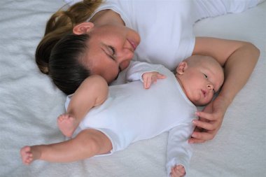 Güzel genç anne yeni doğmuş bebeğiyle yatakta yatıyor. Beyaz elbiseli anne ve oğlunun portresi..