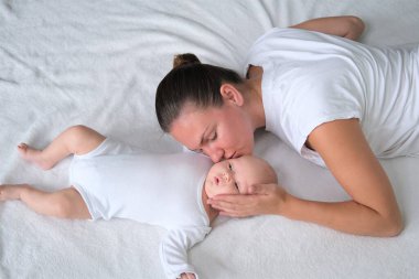 Güzel genç anne yeni doğmuş bebeğiyle yatakta yatıyor. Beyaz elbiseli anne ve oğlunun portresi..