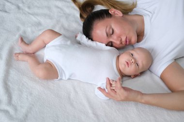 Güzel genç anne yeni doğmuş bebeğiyle yatakta yatıyor. Beyaz elbiseli anne ve oğlunun portresi..