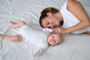 Güzel genç anne yeni doğmuş bebeğiyle yatakta yatıyor. Beyaz elbiseli anne ve oğlunun portresi..