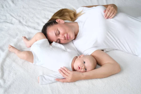 Hermosa madre joven se acuesta con su bebé recién nacido en la cama.Retrato de mamá e hijo en ropa blanca. — Foto de Stock