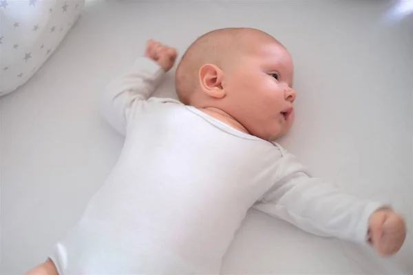 Noworodek w białych ciuchach leży na łóżku. Portret kłamliwego, słodkiego dziecka — Zdjęcie stockowe