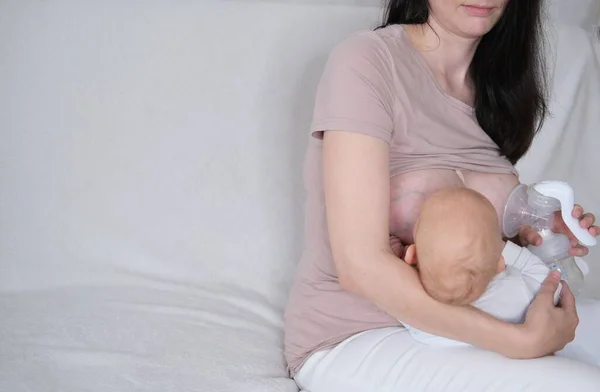 Uma mulher está amamentando seu filho recém-nascido. Mãe bombeia leite em garrafas com uma bomba de mama automática — Fotografia de Stock