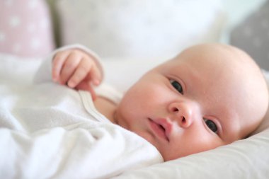  Beyaz elbiseli yeni doğmuş bir bebek yatakta yatıyor. Yalan söyleyen şirin bir çocuğun portresi.