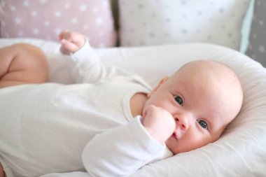  Beyaz elbiseli yeni doğmuş bir bebek yatakta yatıyor. Yalan söyleyen şirin bir çocuğun portresi.