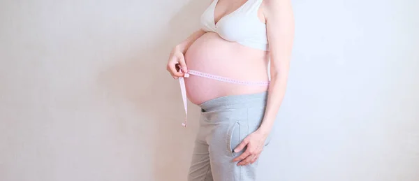 Uma mulher grávida está a medir a barriga. Conceito de excesso de peso. — Fotografia de Stock