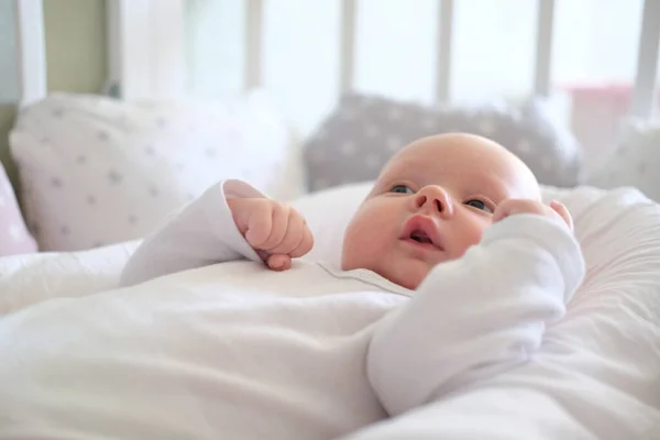 Un neonato in abiti bianchi si trova sul letto. Ritratto di un tenero bambino bugiardo — Foto Stock