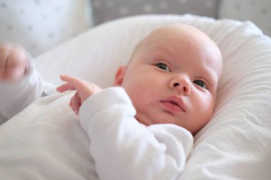 Beyaz elbiseli yeni doğmuş bir bebek yatakta yatıyor. Yalan söyleyen şirin bir çocuğun portresi.