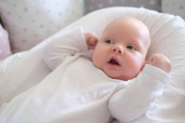 Beyaz elbiseli yeni doğmuş bir bebek yatakta yatıyor. Yalan söyleyen şirin bir çocuğun portresi.