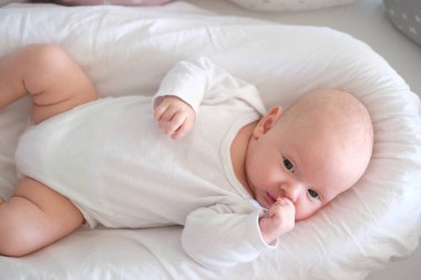  Beyaz elbiseli yeni doğmuş bir bebek yatakta yatıyor. Yalan söyleyen şirin bir çocuğun portresi.