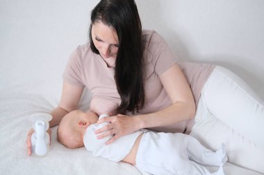 Bir kadın yeni doğan oğlunu emziriyor. Annem şişelere otomatik göğüs pompasıyla süt pompalar.