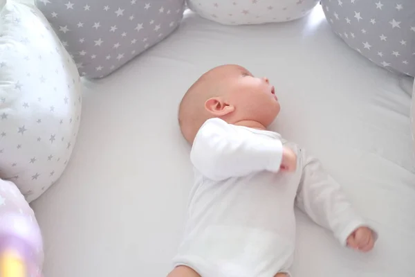 Beyaz elbiseli yeni doğmuş bir bebek yatakta yatıyor. Yalan söyleyen şirin bir çocuğun portresi.