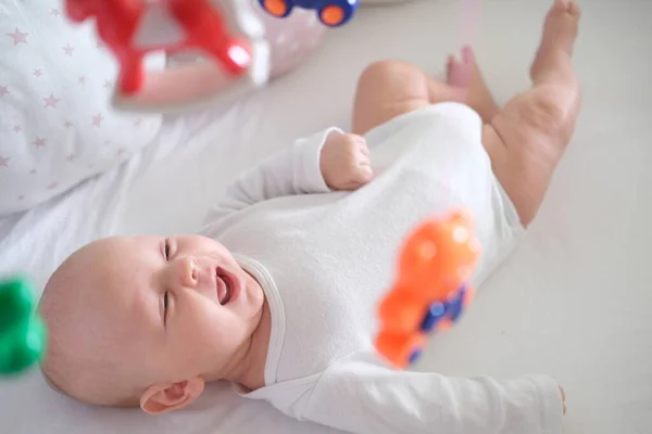 一个穿着白色衣服的新生婴儿躺在婴儿床里，看着他的玩具 — 图库照片