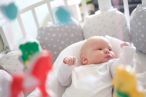 Ein Neugeborenes in weißer Kleidung liegt in der Krippe und betrachtet sein Spielzeug. Baby aus nächster Nähe — Stockfoto