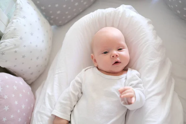 Een pasgeboren baby in witte kleren ligt op het bed. Portret van een liegend schattig klein kind — Stockfoto