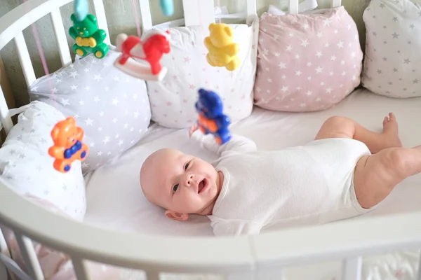 Ett nyfött barn i vita kläder ligger i vaggan och tittar på sina leksaker. Baby leende på nära håll — Stockfoto