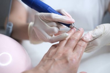 Tırnak bakımı. Usta manikür sırasında ojeli elleri kesmek için elektrikli makine kullanıyor..