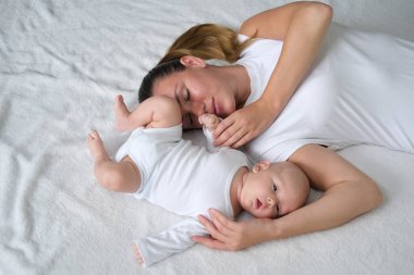 Güzel genç anne yeni doğmuş bebeğiyle yatakta yatıyor. Beyaz elbiseli anne ve oğlunun portresi..