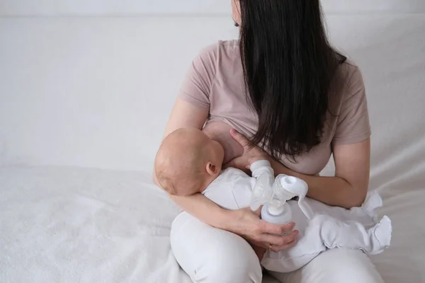 Una mujer amamanta a su hijo recién nacido. Madre bombea leche en botellas con un extractor automático de leche —  Fotos de Stock