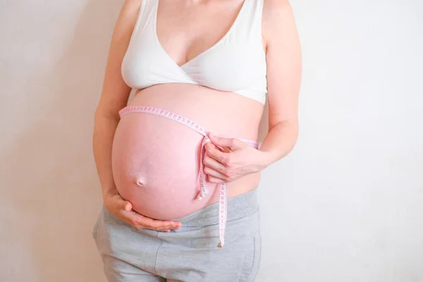 Uma mulher grávida está a medir a barriga. Conceito de excesso de peso. — Fotografia de Stock