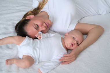 Güzel genç anne yeni doğmuş bebeğiyle yatakta yatıyor. Beyaz elbiseli anne ve oğlunun portresi..