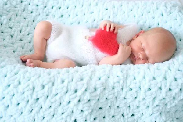 Ein schlafendes Neugeborenes liegt auf blauer Wolle. Herzform rot flauschig weiches Kissen oder Kissen für Valentinstag Liebe — Stockfoto