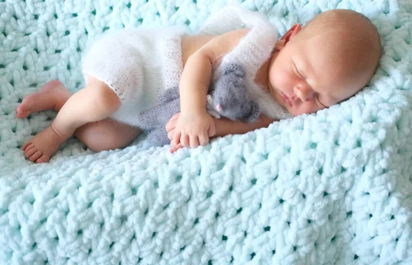 Ett sovande nyfött barn ligger på en blå filt, en virkad leksaksmus i barnens händer — Stockfoto