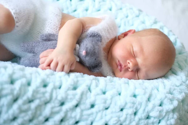 Uyuyan yeni doğmuş bir bebek mavi bir battaniyenin üzerinde yatıyor, bebek ellerinde örülmüş bir oyuncak fare. 