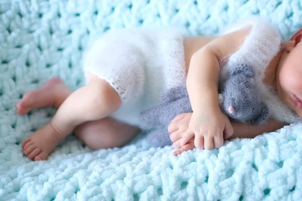 Ett sovande nyfött barn ligger på en blå filt, en virkad leksaksmus i barnens händer — Stockfoto