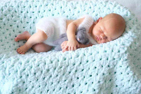 Een slapende pasgeboren baby ligt op een blauwe deken, een gehaakte speelgoedmuis in de babys handen — Stockfoto