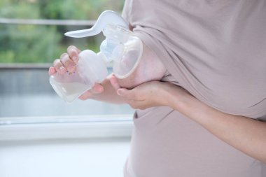 Anne sütünü ifade etmek için elinde makine tutan genç bir kadın. Emzirme kavramı. Göğüs pompası yakın plan.