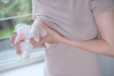 Anne sütünü ifade etmek için elinde makine tutan genç bir kadın. Emzirme kavramı. Göğüs pompası yakın plan.