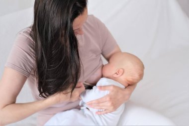 Genç bir kadın yeni doğmuş bir bebeği kollarında tutuyor ve emziriyor. Emzirme konsepti..