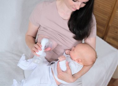 Genç bir kadın yeni doğmuş bir bebeği kollarında tutuyor ve emziriyor..