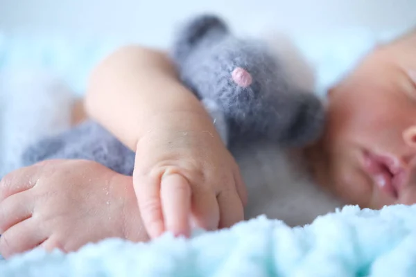 Uyuyan yeni doğmuş bir bebek mavi bir battaniyenin üzerinde yatıyor, bebek ellerinde örülmüş bir oyuncak fare. 