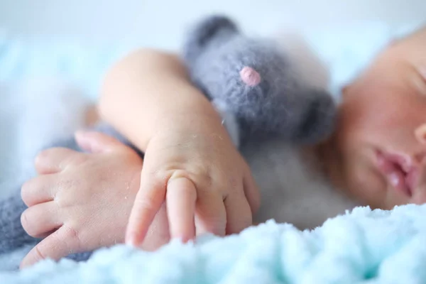 Ett sovande nyfött barn ligger på en blå filt, en virkad leksaksmus i barnens händer — Stockfoto