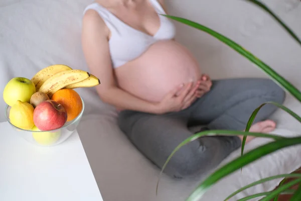 Alimentação saudável, conceito de gravidez. Barriga de uma mulher grávida em um fundo branco e um prato com frutas na mesa — Fotografia de Stock