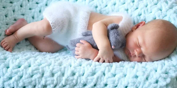 Uyuyan yeni doğmuş bir bebek mavi bir battaniyenin üzerinde yatıyor, bebek ellerinde örülmüş bir oyuncak fare. 