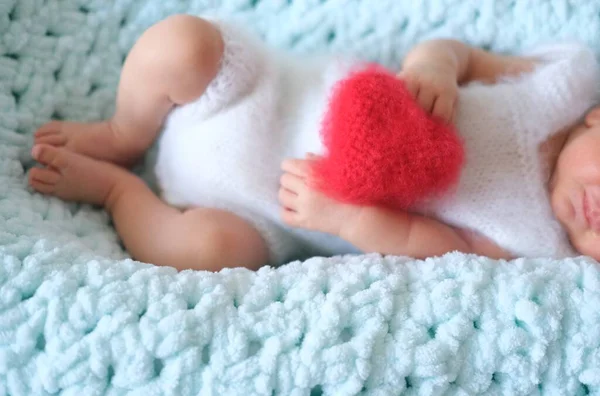 Seorang anak laki-laki yang baru lahir atau perempuan yang sedang tidur terletak di atas wol biru. Hati berbentuk bantal lembut berwarna merah atau bantalan untuk hari kasih sayang di hari kasih sayang — Stok Foto