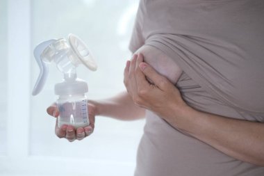Anne sütünü ifade etmek için elinde makine tutan genç bir kadın. Emzirme kavramı. Göğüs pompası yakın plan.