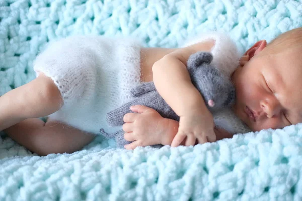 Ett sovande nyfött barn ligger på en blå filt, en virkad leksaksmus i barnens händer — Stockfoto