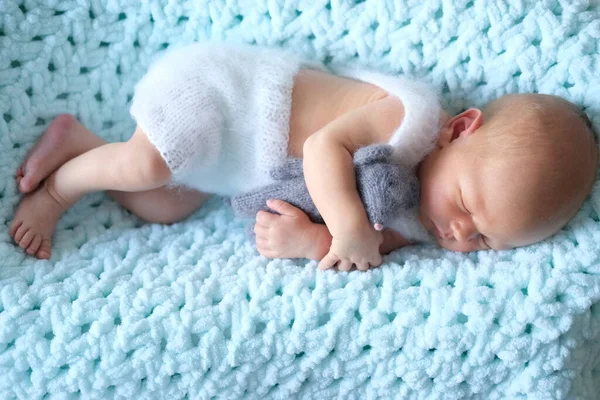 Uyuyan yeni doğmuş bir bebek mavi bir battaniyenin üzerinde yatıyor. Bebek ellerinde örülmüş bir oyuncak fare. 
