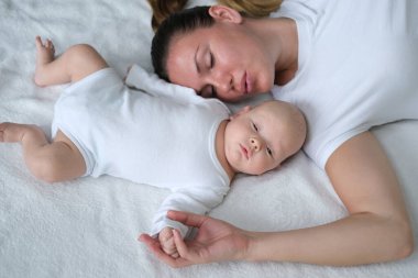 Güzel genç anne yeni doğmuş bebeğiyle yatakta yatıyor. Beyaz elbiseli anne ve oğlunun portresi..