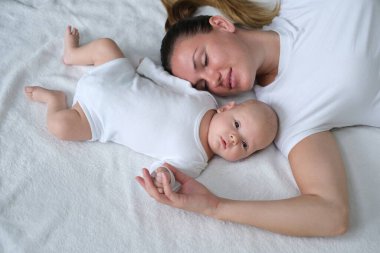 Güzel genç anne yeni doğmuş bebeğiyle yatakta yatıyor. Beyaz elbiseli anne ve oğlunun portresi..