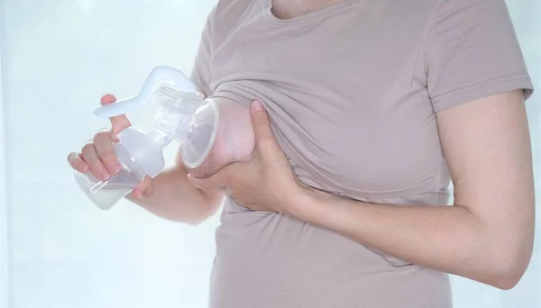 Anne sütünü ifade etmek için elinde makine tutan genç bir kadın. Emzirme kavramı. Göğüs pompası yakın plan.